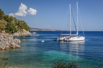 Fototapeta na wymiar White yacht moored in the sea near the rocky coast on a sunny summer day. Holidays in Greece.