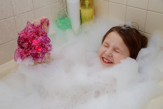 A baby little girl sitting up to their necks in bubbles in the bath have fun blowing bubbles their cupped hands