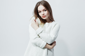 Beautiful long-haired girl in a white knitted sweater is posing on the white background in the studio