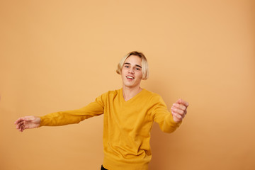 Smiling blond guy dressed in yellow sweater stands on the beige background in the studio