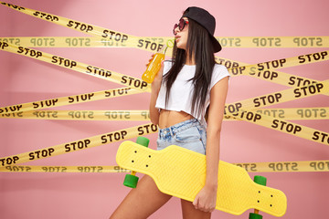 Young girl in pink sunglasses and cap dressed in jeans shorts and white top stands with yellow...