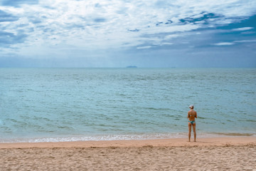 A woman wearing a bikini standing, looking back to the sea