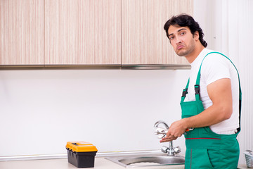 Young plumber repairing tap at kitchen  