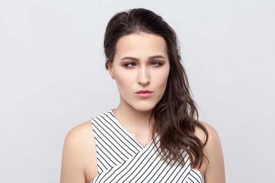 Portrait of crazy funny beautiful young brunette woman with makeup and striped dress standing and looking at camera with crossed eyes. indoor studio shot, isolated on grey background.