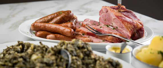 Kassler Nacken, Kohlwurst, Pinkel und Oldenburger Grünkohl auf Platten mit Kartoffeln und Senf auf Marmor Tisch