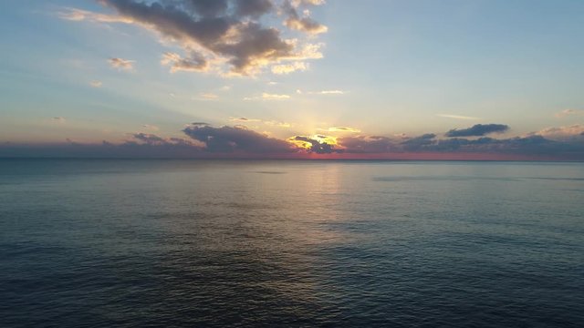 A footage of a sunset from above the sea via drone, clear water and colourfull clouds, 4k resoluted shooting