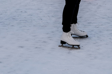 Legs of a woman with white ice skating shoes on ice