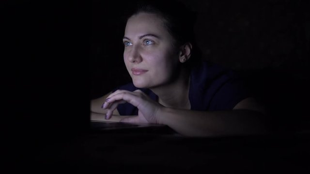 Attractive Girl makes online purchase using a mobile computer lying on a bed at home at night. Isolated light