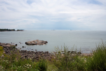 Coast, stones and views of the Gulf of Finland and the island in it on a summer day.