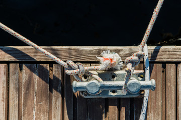 Naklejka premium Yachting detail, rope and mooring double cross bollard on bridge in port of sailing. Wooden pier