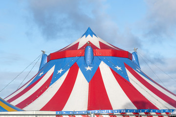 Red and white circus tent topped with bleu starred cover against a sunny blue sky with clouds © Ankor light