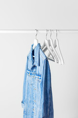 Blue denim jacket on white wooden coat hanger on a rod against light gray wall flat lay copy space. Denim, fashionable jacket, women's or men's trend clothing, fashion background. Store concept, sale.