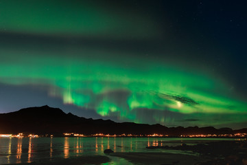 Aurora over sandy beach haukland, Kvalvika and Skagsanden with stones in Norway, Lofoten islands. Northern lights in Lofoten islands, Norway. Starry sky with polar lights. Night landscape with green