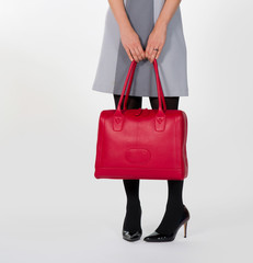 elegantes weibliches Model mit gemustertem Kleid, schwarzer Strumpfhose und schwarzen Highheels hält eine rote Leder Handtasche in den Händen, Detail, Studioshooting