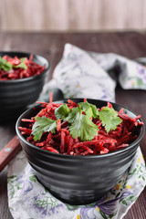 Thinly sliced ​​fresh beets in a black salad bowl with sprigs of cilantro ready for eating are on a wooden table. Shredded beet salad, closeup.