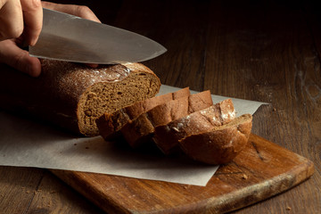 Creative background, male hands cut rye bread close-up, on a wooden cutting board, flat lay, copy space. The concept of fresh pastry, black bread.