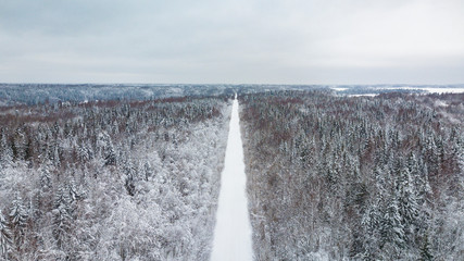 Aerial view of country road going through the beautiful snow covered landscapes.