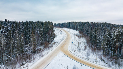 Aerial view of winter road between forest trees.