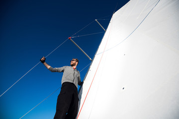 Yacht captain with a beard stands on sail boom on a sailing yacht, holding the rope in his hand and...