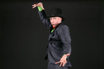 The magician with a bowler hat above his head is casting a magic spell on black background.