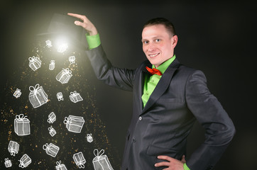 The magician is holding a magic bowler hat from which is dropping a present gift boxes on black...