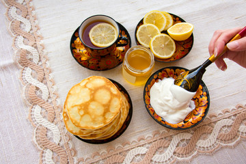 tea in a painted Cup, on a saucer sliced lemon, pancakes, sour cream and a wooden spoon for overlaying. tea party in rustic style