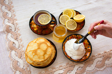 tea in a painted Cup, on a saucer sliced lemon, pancakes, sour cream and a wooden spoon for overlaying. tea party in rustic style
