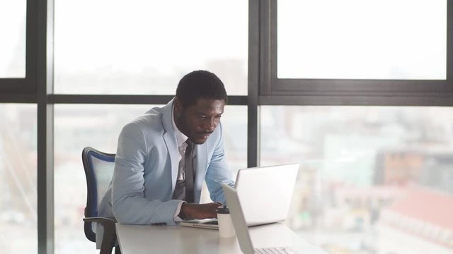 Successful African bearded entrepreneur in sky blue coat and tie serfing web sites with attentive and concentrated look, searching useful information