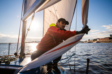 Handsome man on yacht touches white sail called assymetric spinnaker, works with tackle in sea at...
