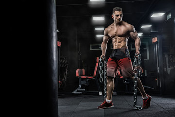 Fototapeta na wymiar Young handsome male athlete bodybuilder does exercises for leg muscles, uses chains. Beautiful dark background. Concept - gym sports nutrition diet styroyd health simulators strength power crossfit.
