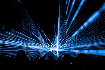 Blue laser show nightlife club stage with party people crowd. Luxury entertainment with audience silhouettes in nightclub event, festival or New Year's Eve. Beams and rays shining colorful lights