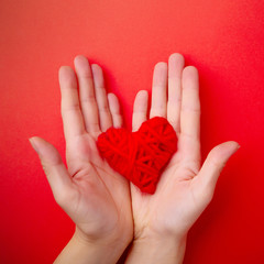 Hands hold red heart on red background