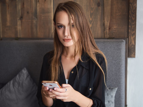 Beautiful woman reading good news on mobile phone during rest in coffee shop. Happy caucasian female watching photos on smartphone checking social networks while relaxing in cafe during free time