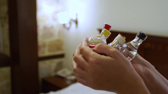 Closeup side view of two female hands holding several small bottles with alcohol drinks standing in room of hotel or home. Real time 4k video footage.