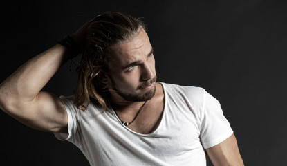 Naklejka premium Portrait von einem jungen Mann mit Bart und langen Haaren in skeptischer nachdenklicher Pose, Studio, dunkler Hintergrund