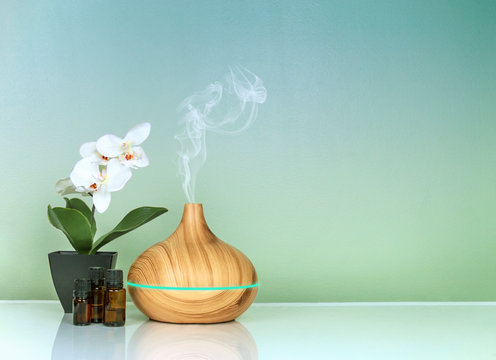 Electric Essential oils Aroma diffuser, oil bottles and flowers on green blue gradient surface with reflection