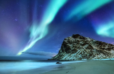Fototapeta na wymiar Aurora borealis on the Lofoten islands, Norway. Green northern lights above mountains and ocean shore. Night winter landscape with aurora and reflection on the water surface. 