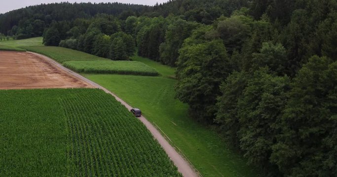 Aerial of an american SUV car driving in rural landscape throuh corn fields on a bright sunny day in bavaria germany 