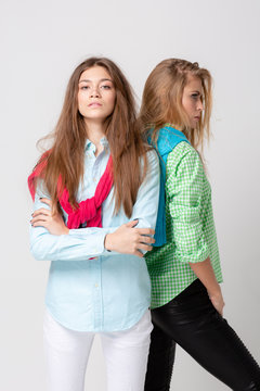 happy girlfriends women in shirts and a sweater on his shoulders. Fashion spring image of two sisters. Colorful colors clothes. Models with Blonde and light brown hair. Looking at camera and smiling.