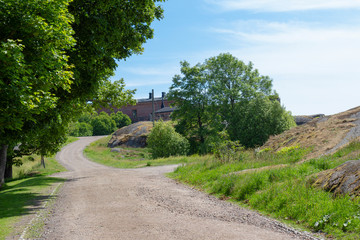 Fototapeta na wymiar Country road, trees and old buildings are part of the natural Finnish landscape on Suomenlinna Island in Finland on a summer day.