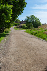 Fototapeta na wymiar Country road, trees and old buildings are part of the natural Finnish landscape on Suomenlinna Island in Finland on a summer day.