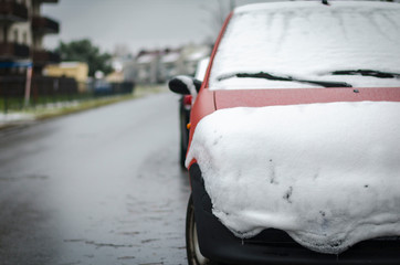 Obraz premium Red car covered with snow along the road. Concept of winter, snowfall