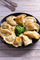 Fried dumplings stuffed with meat and served with chopped parsley and spring onion on a black plate on a wooden rustic table