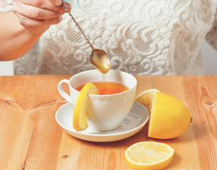 cup of tea with a lemon on a wooden table to which a spoon add honey