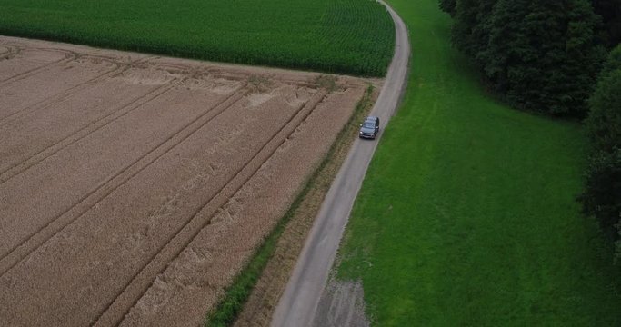 Aerial of an american SUV car driving in rural landscape throuh corn fields on a bright sunny day in bavaria germany 