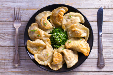 Fried dumplings stuffed with meat and served with chopped parsley and spring onion on a black plate on a wooden rustic table. View from above, top studio shot