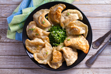 Fried dumplings stuffed with meat and served with chopped parsley and spring onion on a black plate on a wooden rustic table. View from above, top studio shot