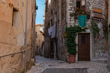 Fototapeta na wymiar A narrow traditional street paved with stone among stone houses in a medieval small town Sermoneta not far from Rome. Launry is drying in the street and flowers are planted beneath the opened window