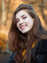 Naklejka premium Fabulous redhead woman with long hair in yellow sweater black leather jacket on blurred autumn background.