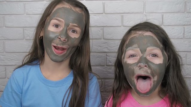 Funny children with clay mask. Cheerful little girls with a clay mask on their faces show their tongues. Funny kids fooling around.